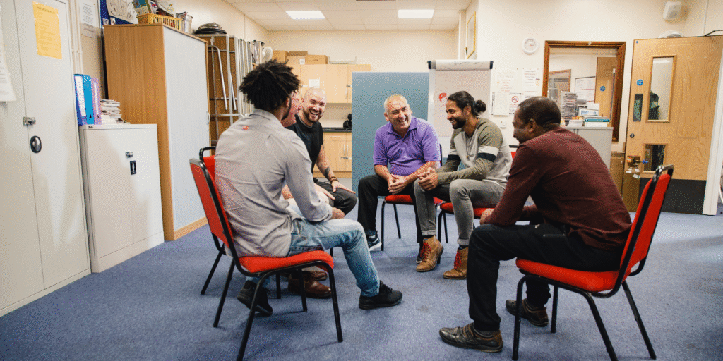 A group of men sitting in a support circle, discussing how to overcome setbacks in life together.